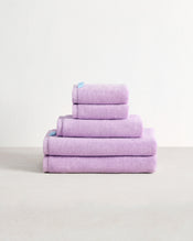A stack of four Violet 100% Cotton Terry Bath Towels by Bed Threads, in assorted sizes, is neatly folded in a pyramid shape on a light surface with a plain white background. - view